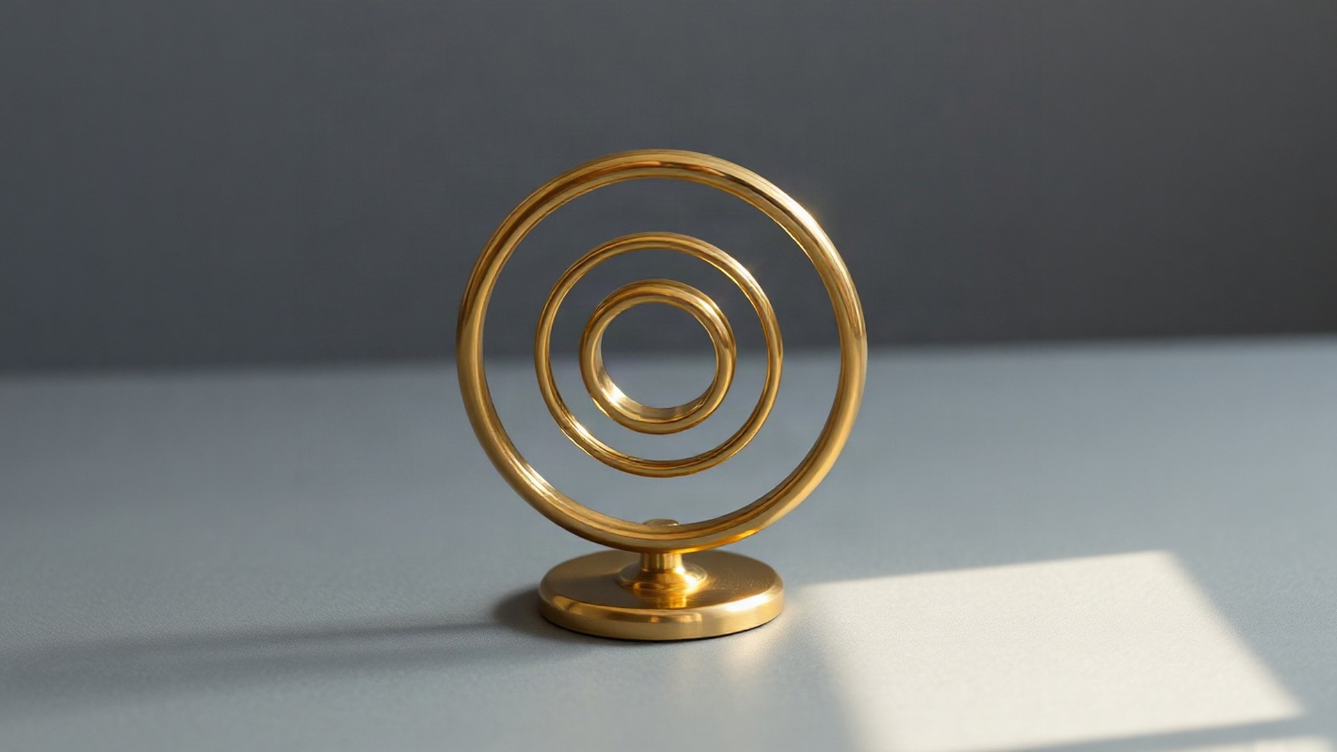 A polished brass gyroscope of three concentric gimbal rings stands upright on a plain matte slate-grey surface, the kind of instrument that measures steady rotation rather than sudden turns. Photo: The Signal / AI-generated.