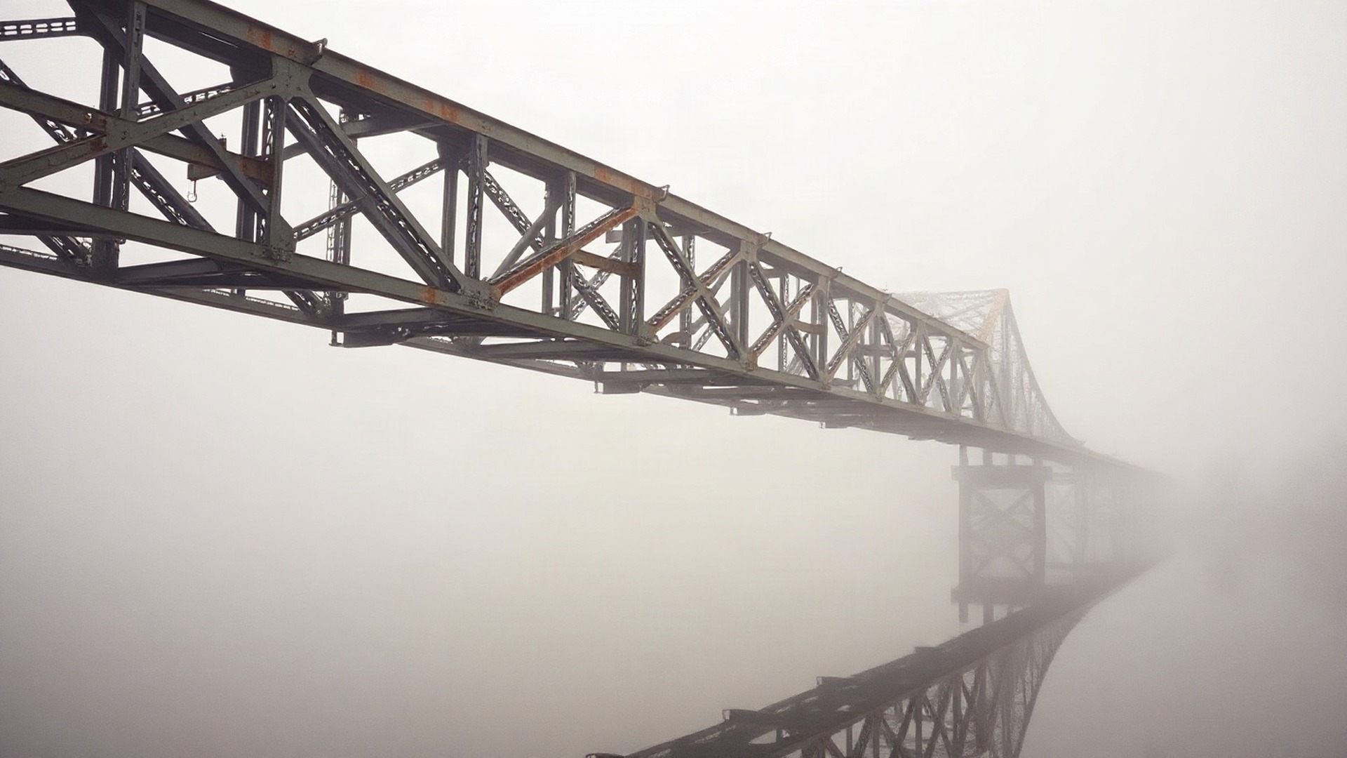 A weathered steel truss bridge fades into dawn fog over still water, the kind of long-lived physical asset an infrastructure fund owns through its holdings. Photo: The Signal / AI-generated.
