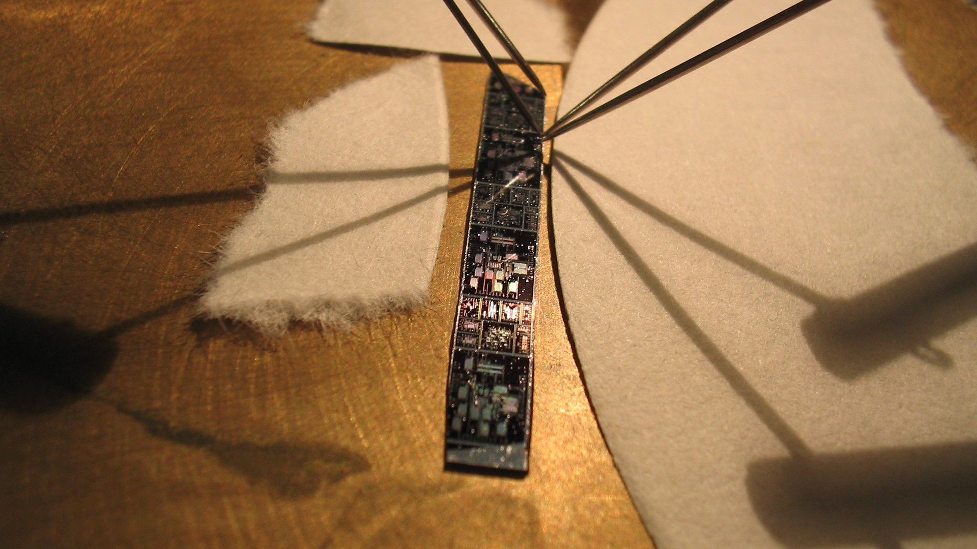 Fine metal probe needles make contact with a strip of silicon dies on a test bench - the verification step every chip has to clear before it ships, which is the layer Synopsys' tools own. Photo: Iuri Kothe / Wikimedia Commons, CC BY 2.0